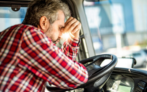 Distraught truck driver leaning on a steering wheel and having a headache.