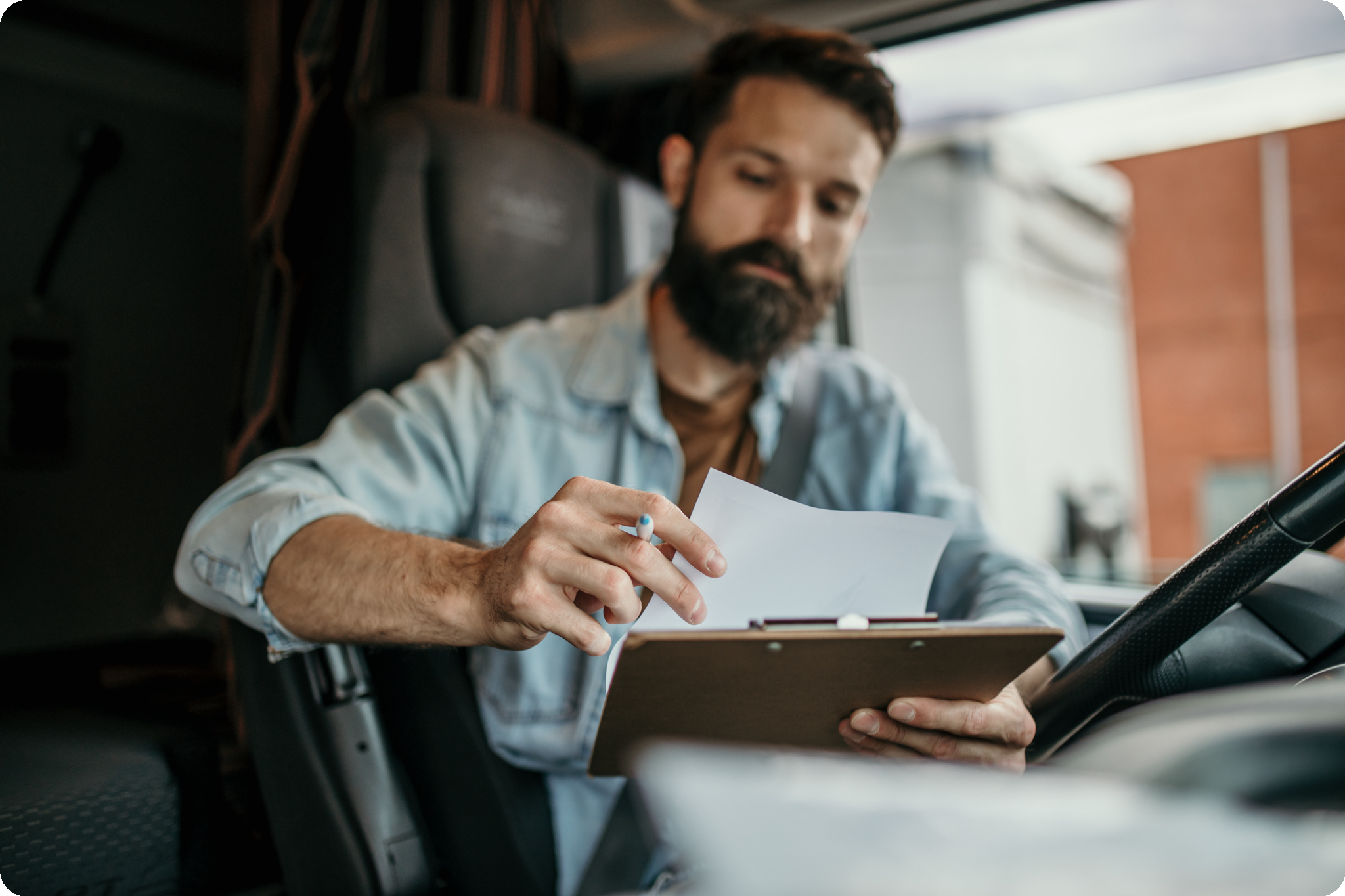rounded_image Truck driver reviewing paperwork on a clipboard inside a semi truck cab while preparing for operating authority registration